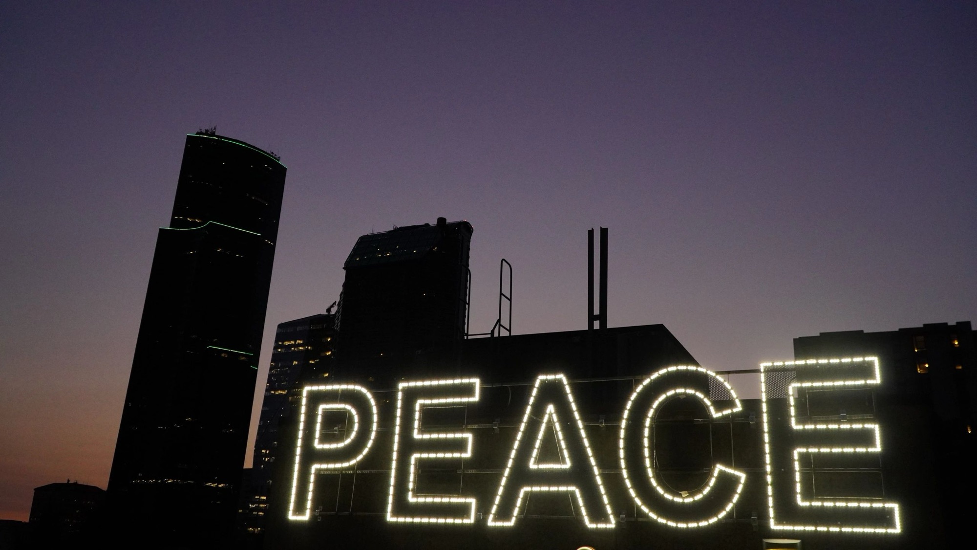PEACE sign glowing against a night city skyline